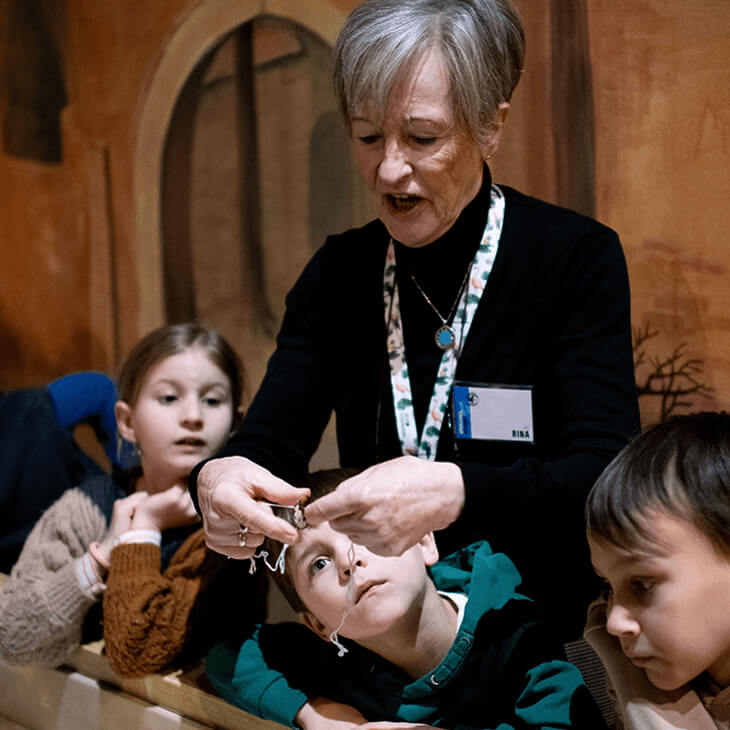 De gids toont de leerlingen de zelfgemaakte zoemschijf tijdens hun klasbezoek aan het Speelgoedmuseum