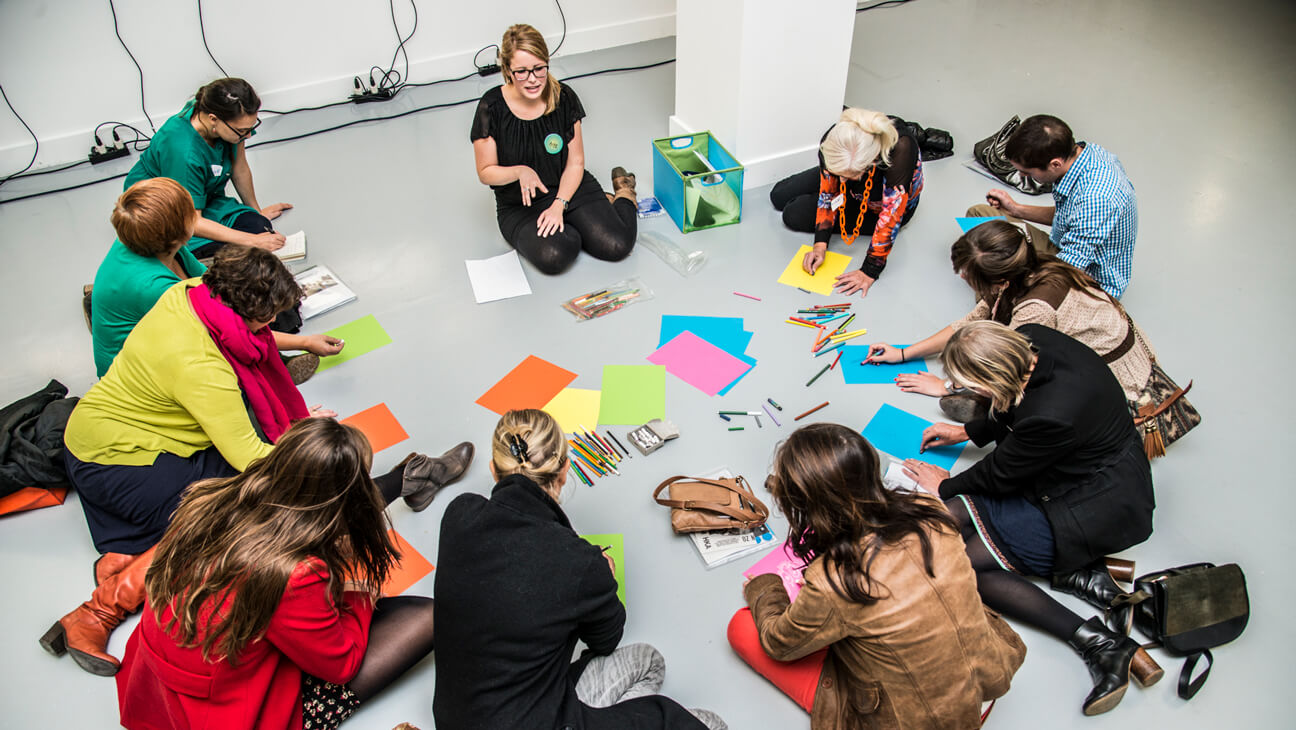 Groep leraren op de grond met papieren en schrijfgerief in M HKA