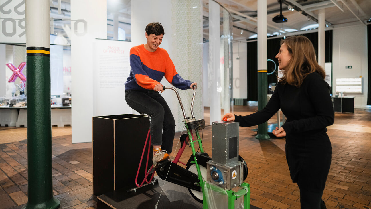 Bezoekers op een hometrainer op de expo 'Plastic Fantastic'